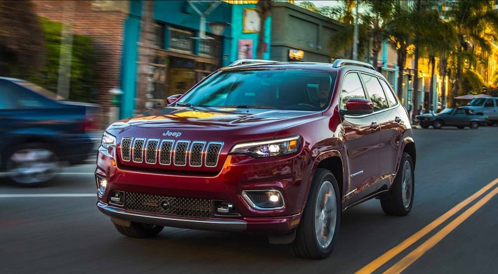A burgundy 2019 Jeep Cherokee is driving downtown.