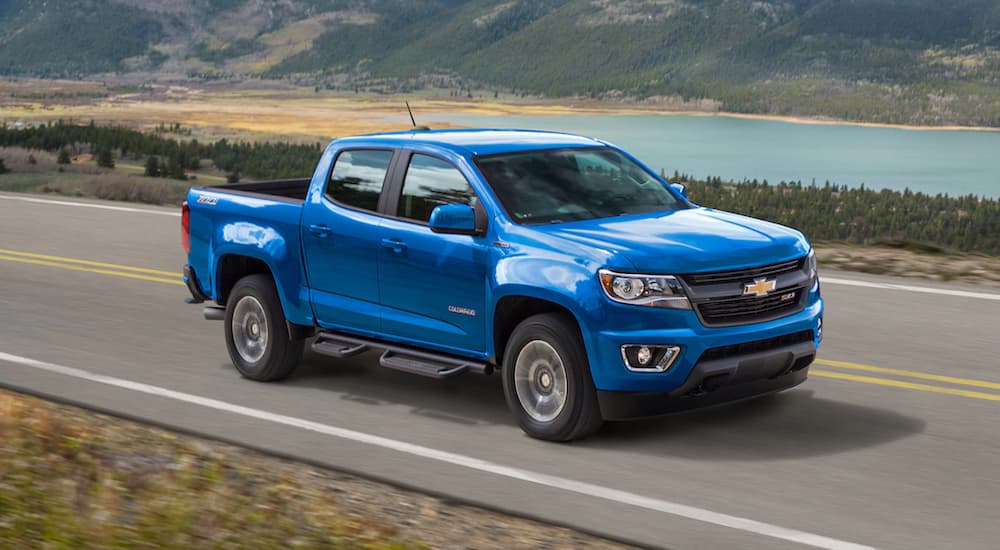 A blue 2019 Chevy Colorado, one of the popular trucks for sale, is driving with a lake in the distance.