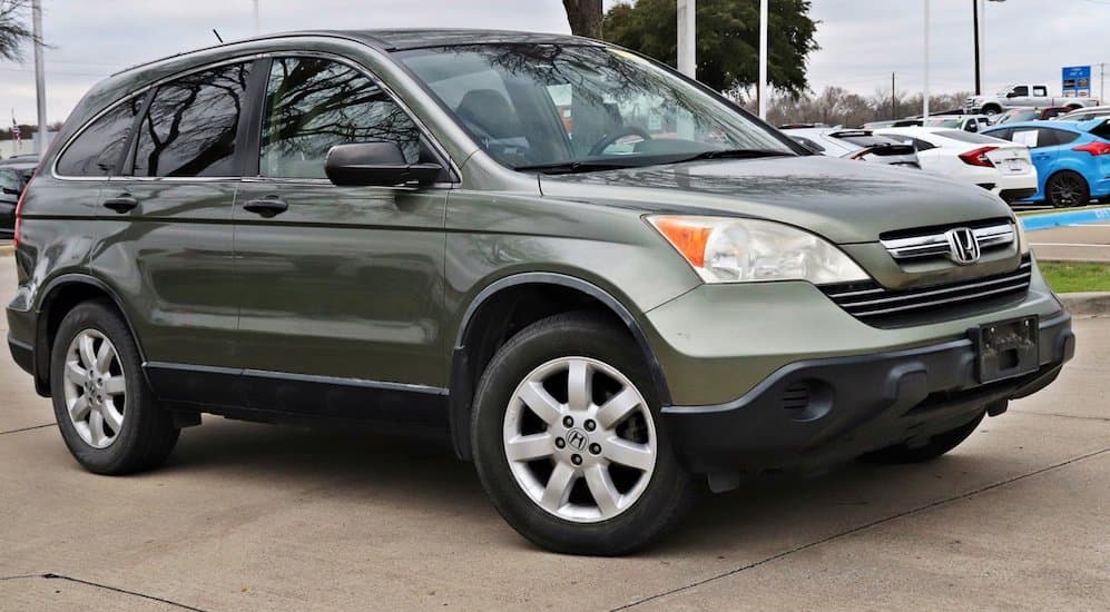 A 2009 green Honda CR-V is parked near a dealership on a cloudy day.