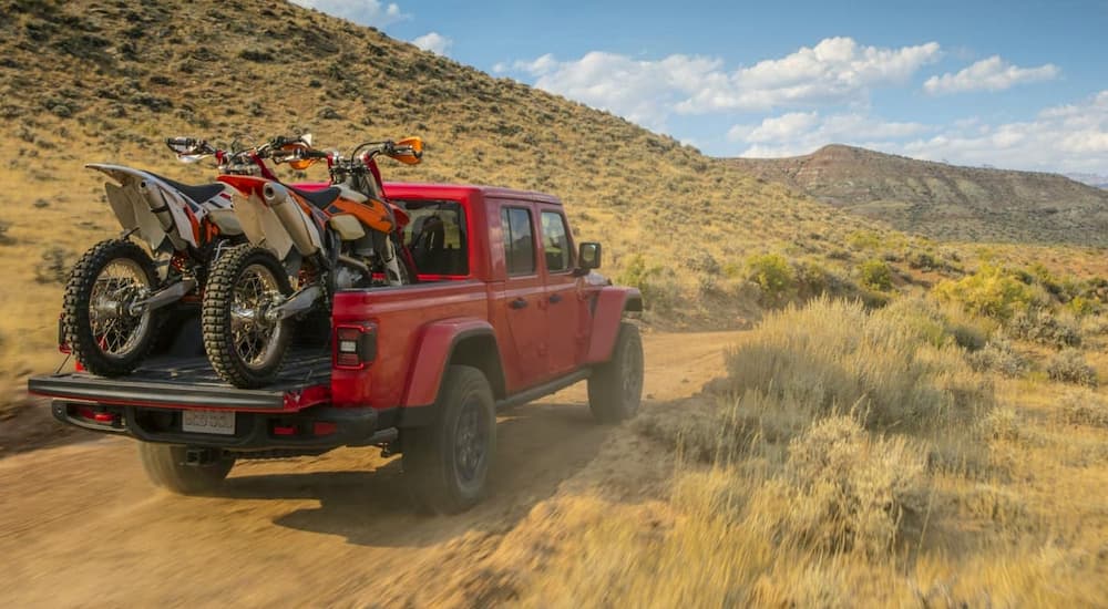 A red 2020 Jeep Gladiator is driving on a dusty trail with dirt bikes in the bed.
