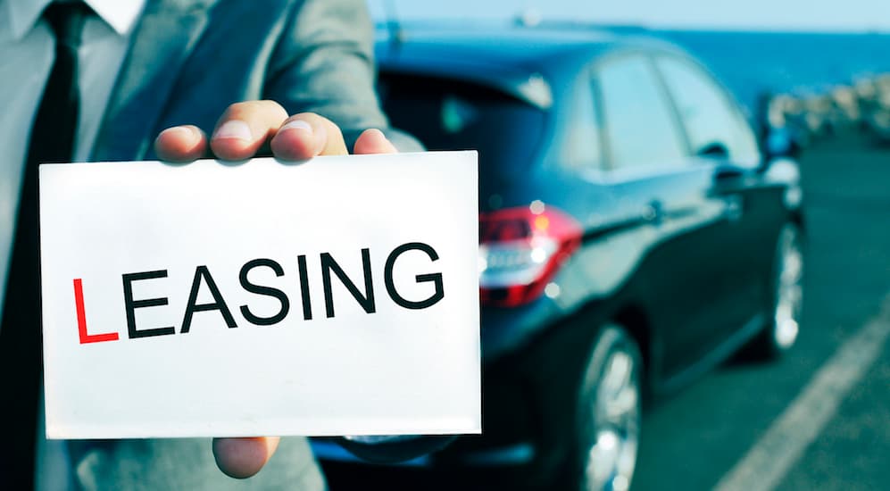A salesman is holding a leasing sign in front of a new car. Searching ' Kia lease deals', will help you find local deals. 