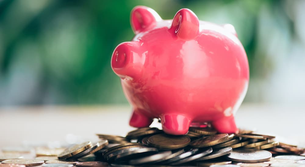 A piggy bank on top of coins is shown because it is important to know what you can afford when looking at bad credit car finance options.
