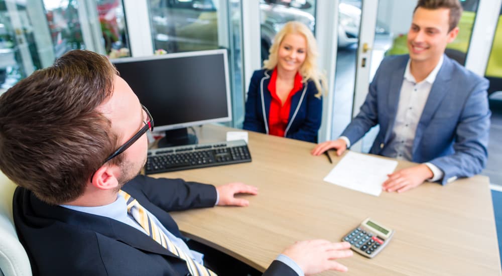 A salesman is talking to a couple at his desk at a Buy Here Pay Here dealership.