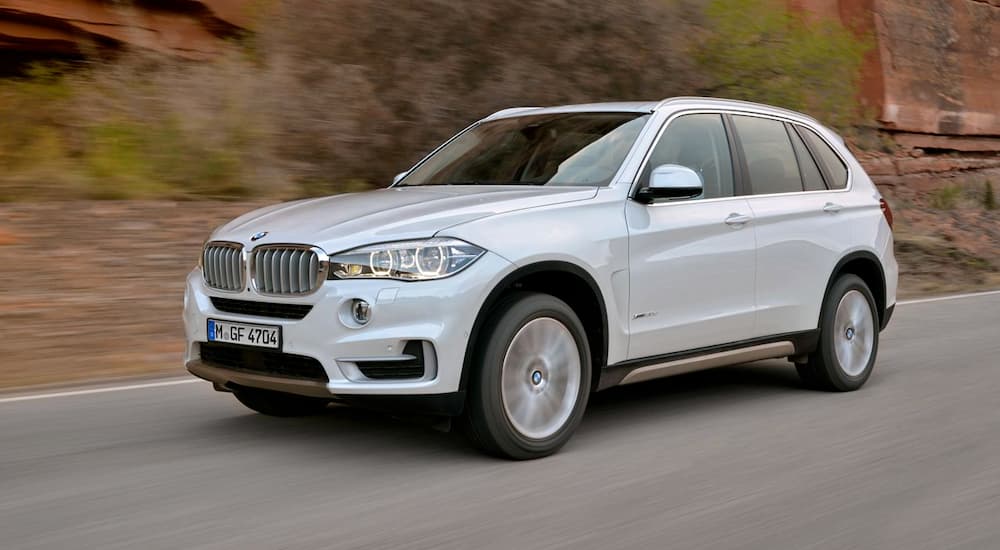 A white 2014 BMW X5 is driving past a blurred rock background.