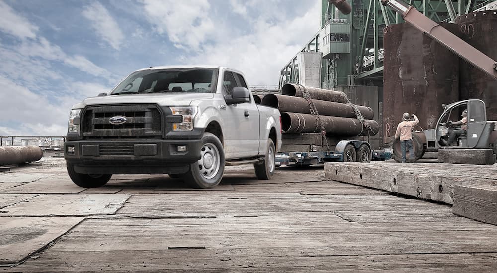 A 2015 Ford F-150 is shown towing a trailer with industrial pipes loaded on it. 