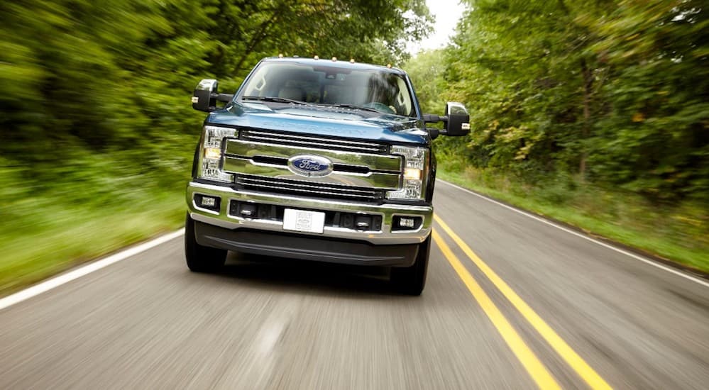 A blue 2017 Ford F-250, popular among used Ford trucks in Columbus, is cruising down a road with trees on both sides.