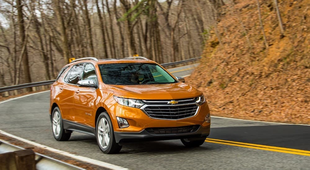 An orange 2019 Chevy Equinox is driving on a road with trees in the background. 