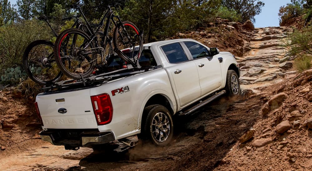 A white 2019 Ford Ranger is climbing a rock hill with bikes on the bed rack.