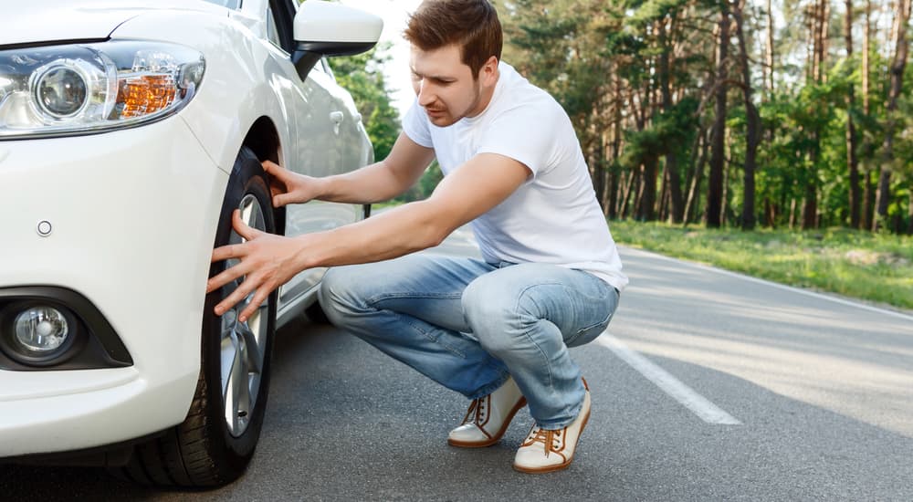 A man is checking the tire on his white car because poor alignments can cause issues.