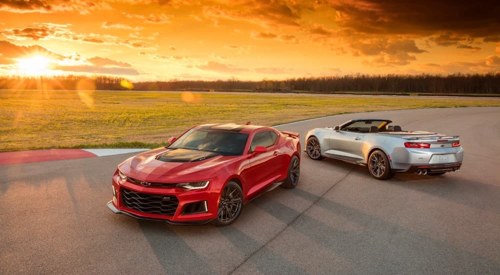 A silver 2018 Chevy Camaro is parked next to a red ZL1 with a sunset behind them.
