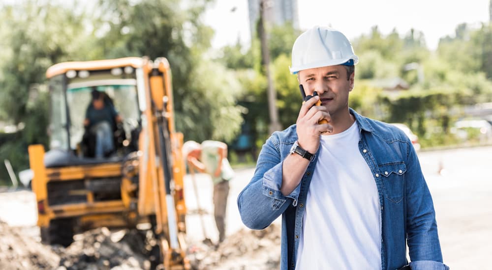 A construction worker is talking on a walkie-talkie in an area where many commercial vehicles will be passing.