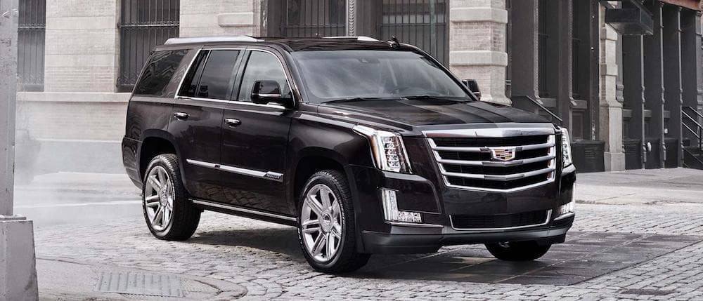 A black used Cadillac Escalade parked on a small city street. 