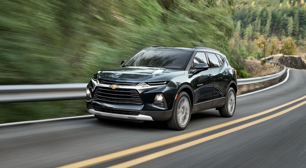 A dark graphite 2019 Chevy Blazer is driving on a tree-lined road.