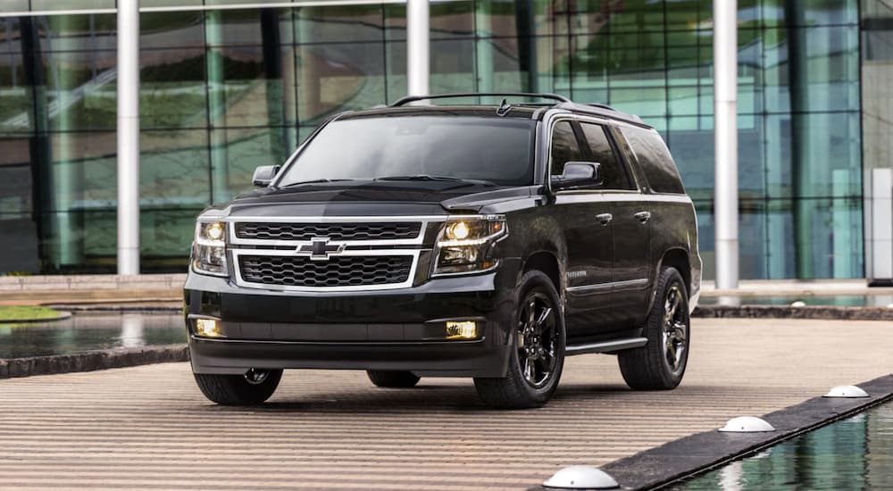 A blacked out 2019 Chevy Suburban is parked in front of a glass building.