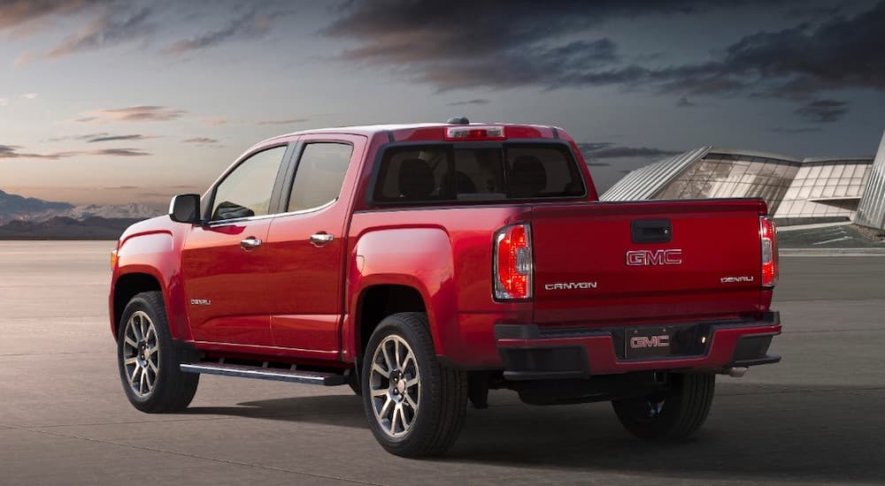 A red 2019 GMC Canyon, which wins when comparing the 2019 GMC Canyon vs 2019 Honda Ridgeline, is in front of a glass building.