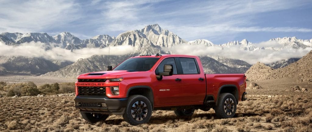 A red 2020 Chevy Silverado 2500HD is parked on dirt with snowy mountains behind it. 