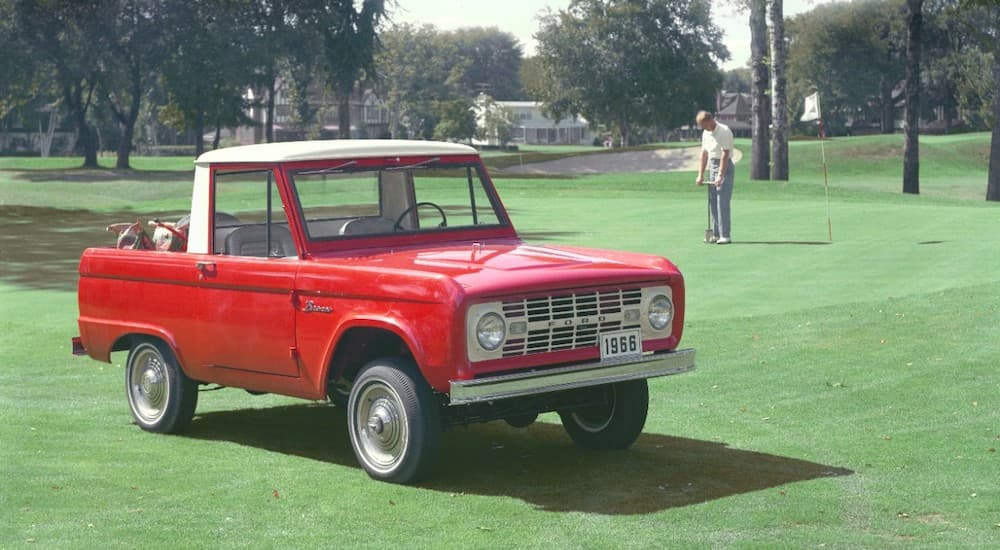 A red 1966 Ford Bronco is on a golf course.