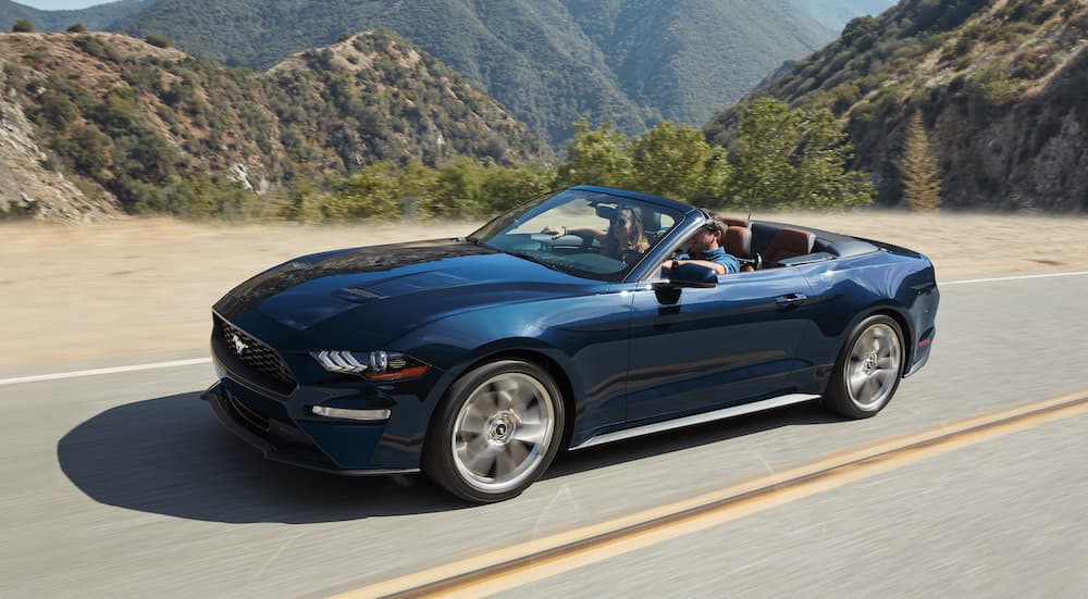 A blue convertible 2019 Ford Mustang, a popular new Ford for sale, is driving past mountains.