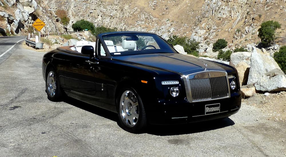 A black Rolls-Royce Phantom Drophead Coupe is parked in front of rocky hills.
