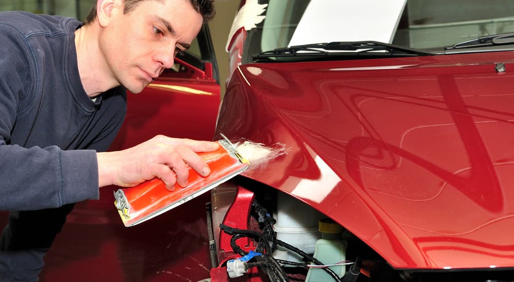 A man is doing body work on a damaged red car.