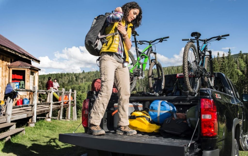 A woman is on the tailgate of a 2015 Chevy Colorado loading bike gear.
