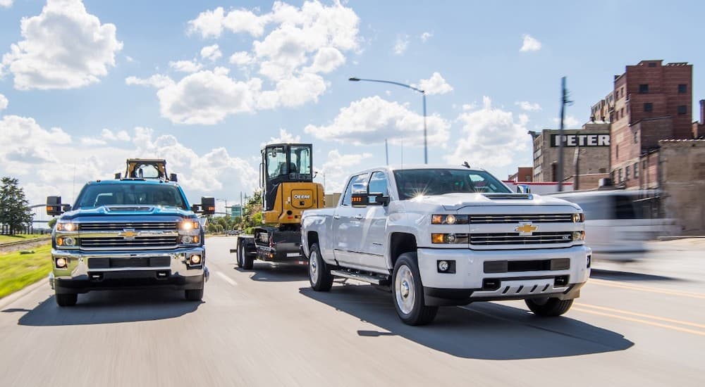 Two 2017 Chevy Silverado 2500HDs, popular used trucks for sale, are towing machinery.