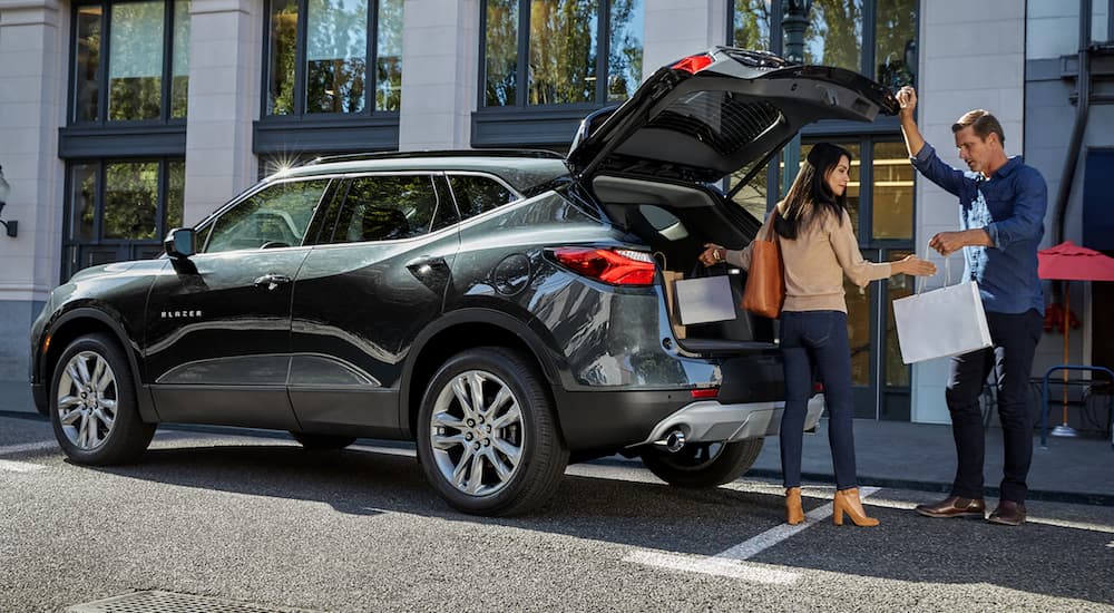 A dark colored 2019 Chevy Blazer is parked on a city street while a couple loads shopping bags.