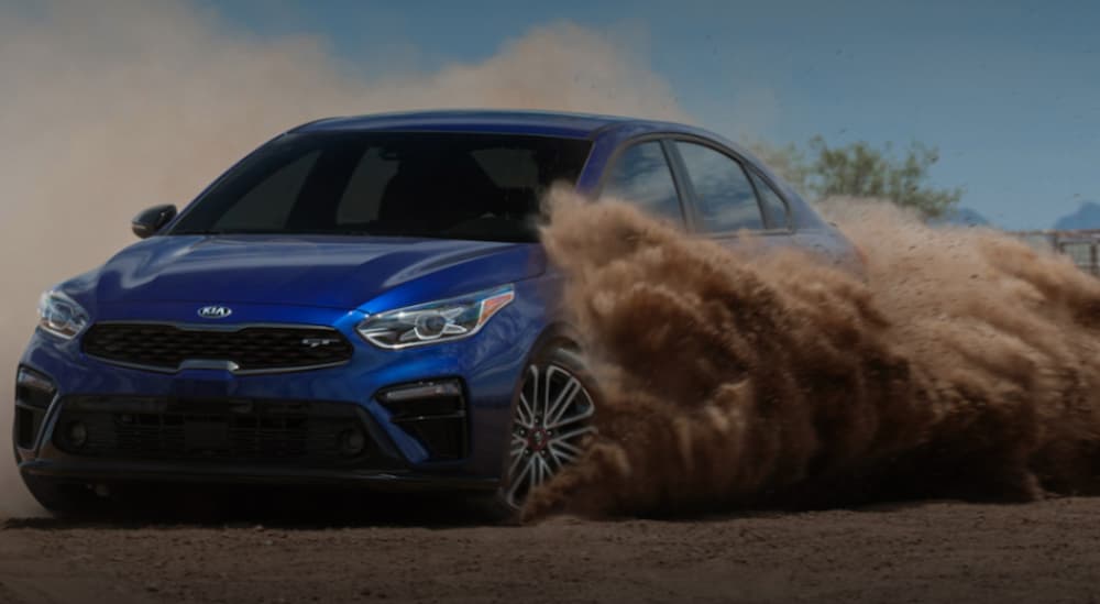 A blue 2020 Kia Forte GT is drifting with a dirt cloud behind it.