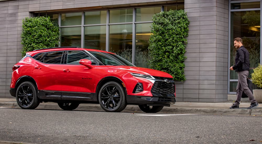 A man is walking towards his red 2019 Chevy Blazer on a city street.