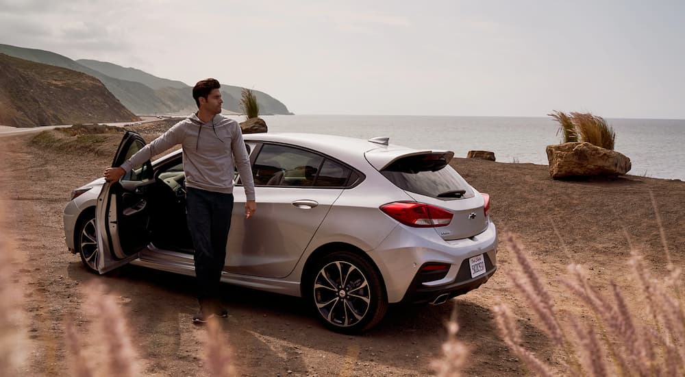 A man is closing the door of his 2019 Chevy Cruze at the beach.