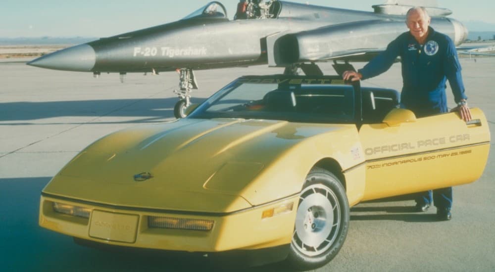 Chuck Yeager is next to the yellow 1986 Corvette Pace Car in front of a fighter jet.