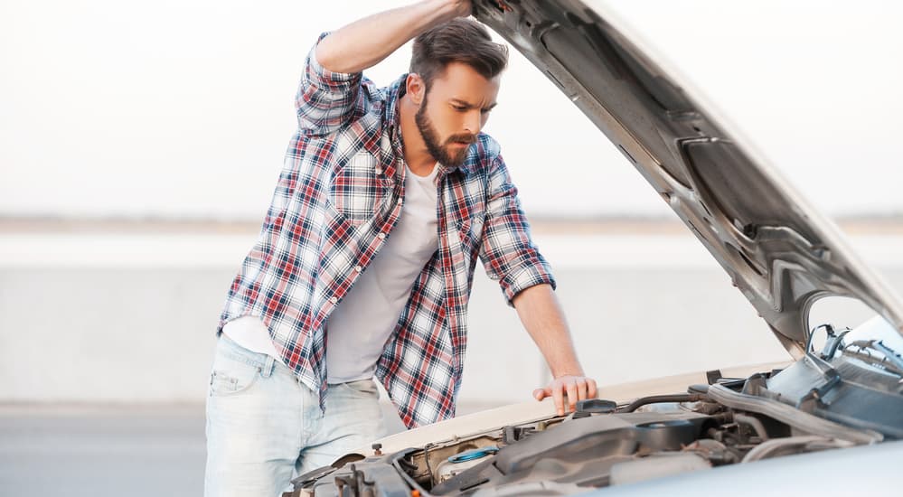 A man is looking under the hood of a used car he's looking at buying. 