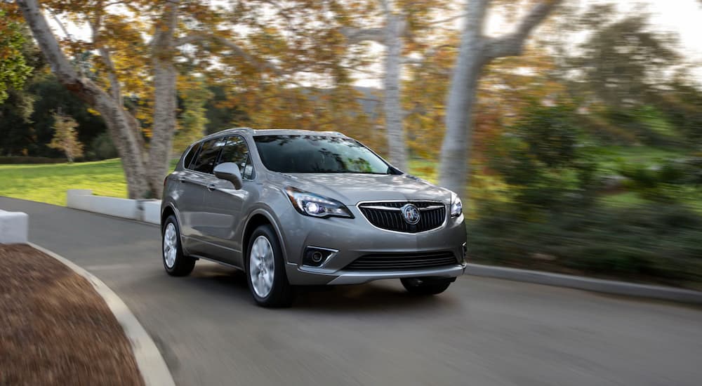 A grey 2020 Buick Envision is driving on a treelined road. 