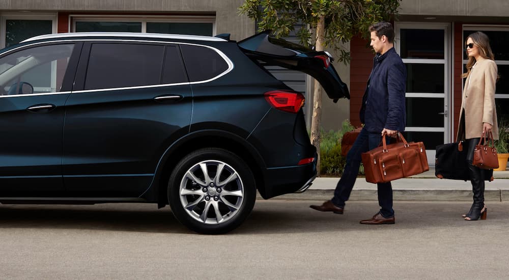 A smiling couple is using the easy to use Liftgate feature to open the tailgate of their Envision. 