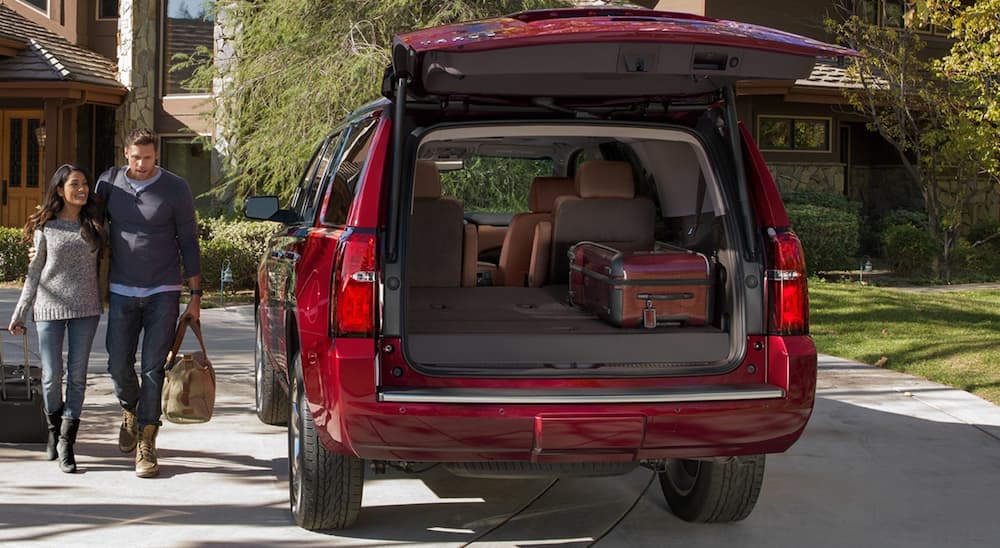 A smiling couple is loading suitcases in the back of their red 2020 Chevy Tahoe.