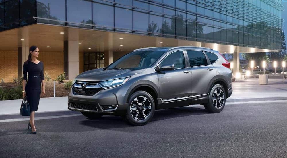 A smiling woman is walking to her grey 2019 Honda CR-V that parked in front of an office building.