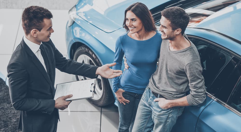 A salesman at one of your local Atlanta used car dealerships is shown with smiling customers.