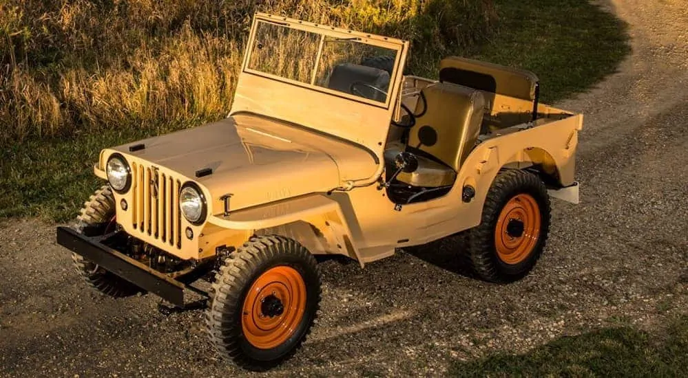 A birds eye view of a tan 1945 Jeep CJ-2A is parked on a dirt trail at dusk.
