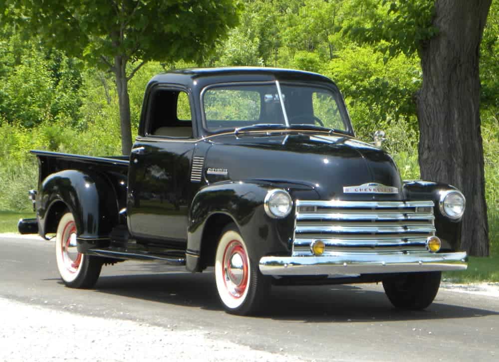 A black 1947 Series 3100 Pickup is parked on a treelined road.
