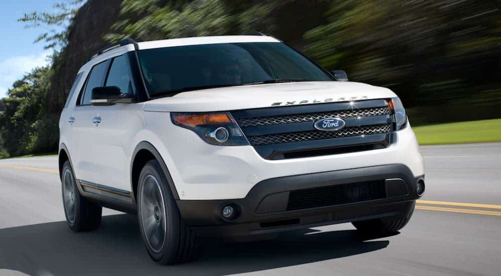 A white 2015 Ford Explorer is driving on a road past blurred trees.