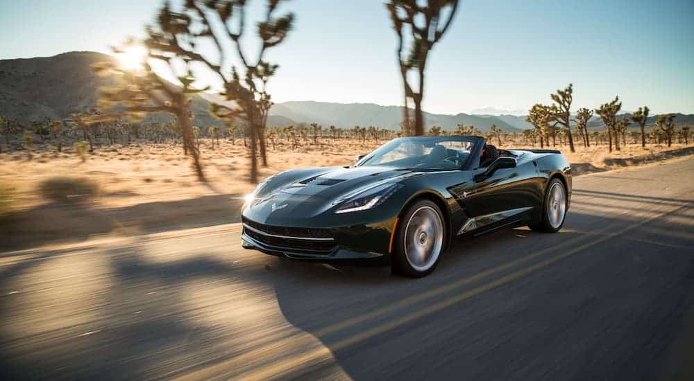 A black 2018 Chevy Corvette, which is popular among used cars with great performance, is driving on a road through the desert on a sunny day. 