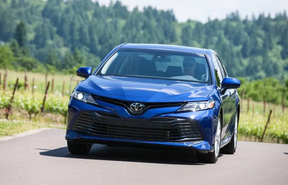 A blue 2019 Toyota Camry is driving on a grass lined road. 
