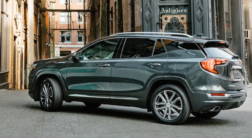 A side view of a grey 2019 GMC Terrain, which wins when comparing the 2019 GMC Terrain vs 2019 Nissan Rogue Sport, is parked next to old brick buildings.