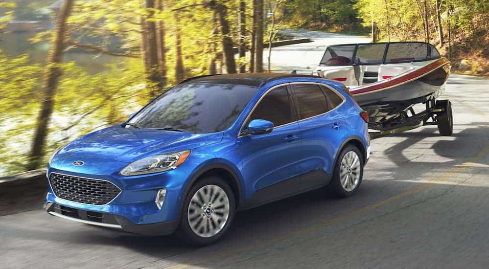 A blue 2020 Ford Escape, which wins when comparing the 2020 Ford Escape vs 2020 Kia Sportage, is towing a boat on a windy treelined road.