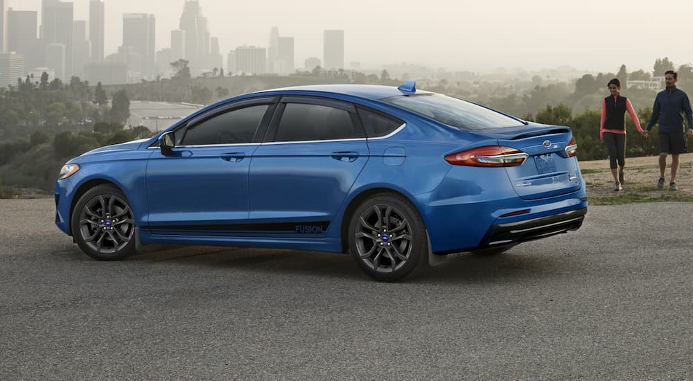 A blue 2020 Ford Fusion, which wins when comparing the 2020 Ford Fusion vs 2019 Ford Fusion, is parked near a city park.