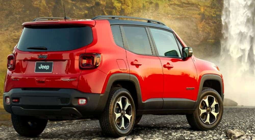A red 2020 Jeep Renegade, which wins when comparing the 2020 Jeep Renegade vs Honda HR-V, is parked on rocks while facing a waterfall in the woods.