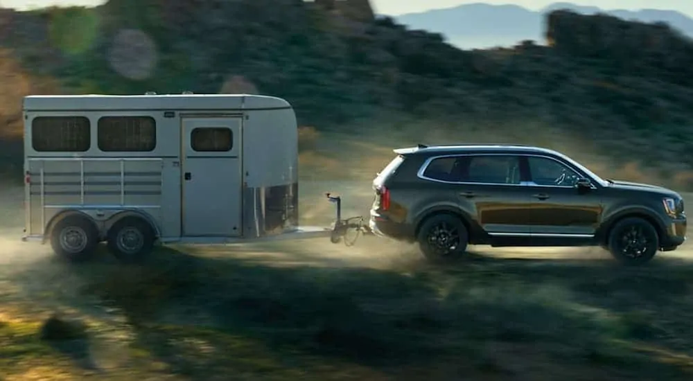 A side view of a 2020 KIA Telluride towing a horse trailer with large rock hills in the background. 