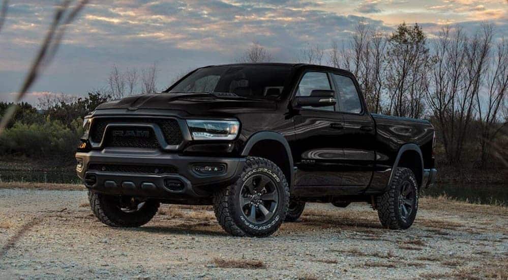 A black 2020 Ram 1500 Rebel is parked on an open dirt trail next a grassy field at dusk. 