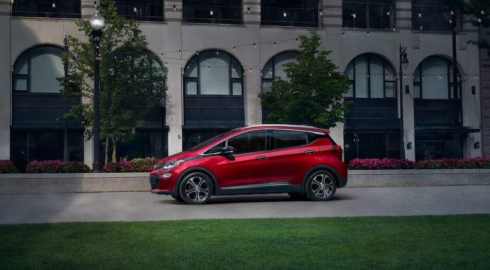 A red 2020 Chevy Bolt EV is parked in front of a white brick building and trees