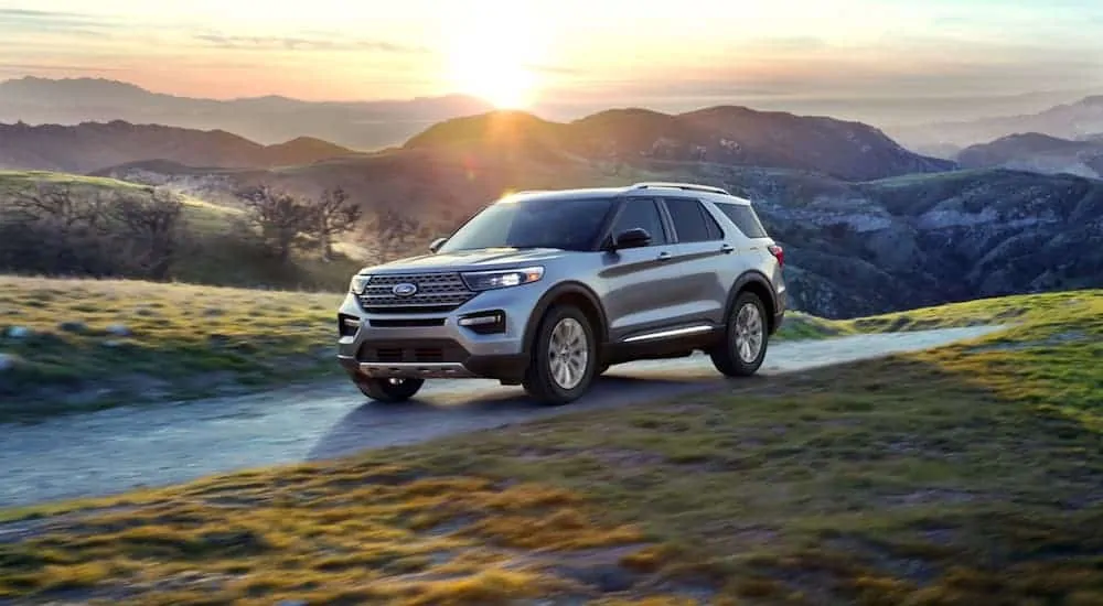 A grey 2020 Ford Explorer is driving with mountains and a sunset behind it.